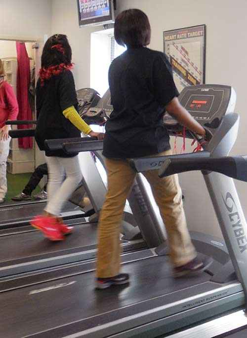 Two students enjoy chatting while walking on the Fitness Room treadmills.
